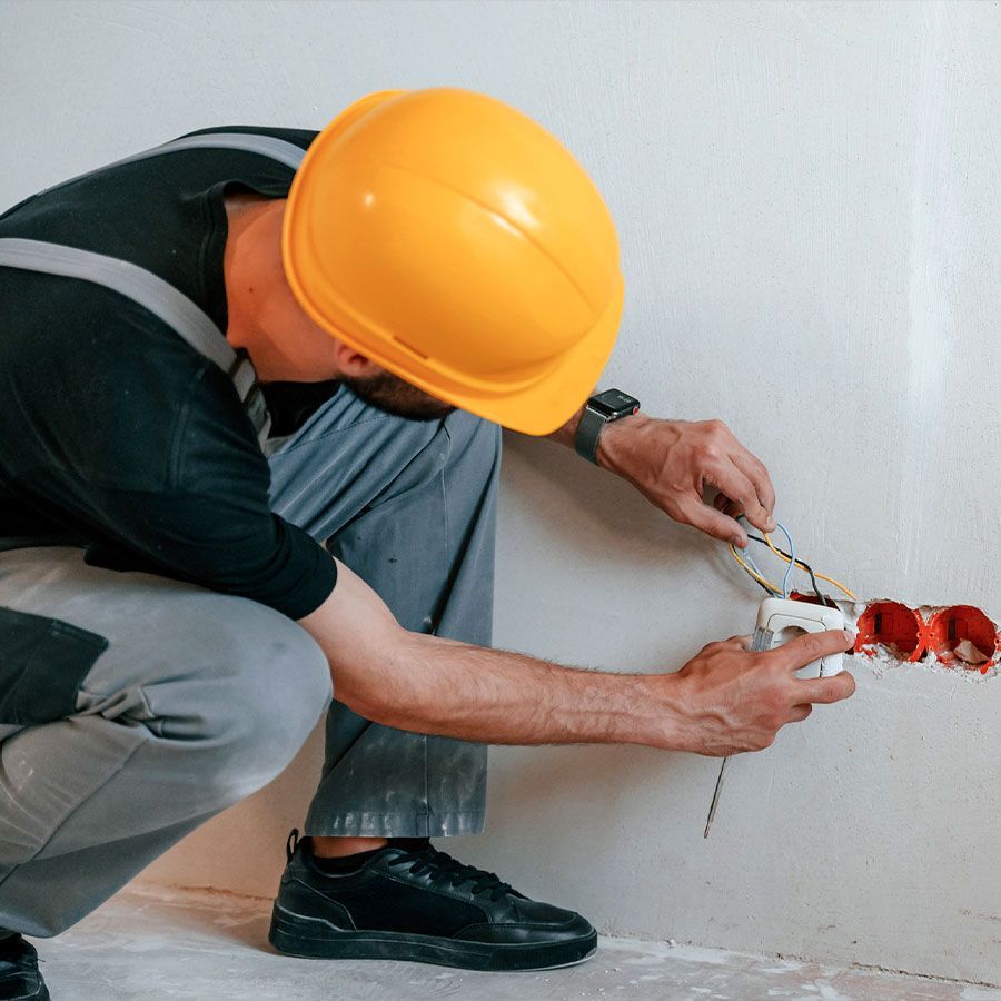 Un hombre que lleva un casco de seguridad está trabajando en una toma de corriente eléctrica.