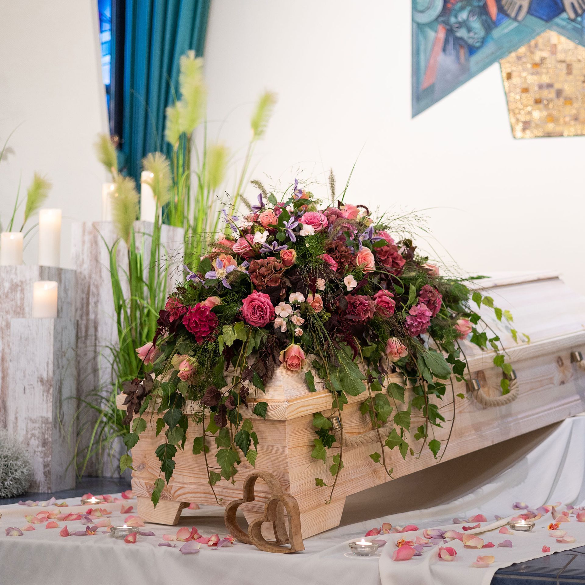Holzsarg mit Blumenarrangement und Kerzen.