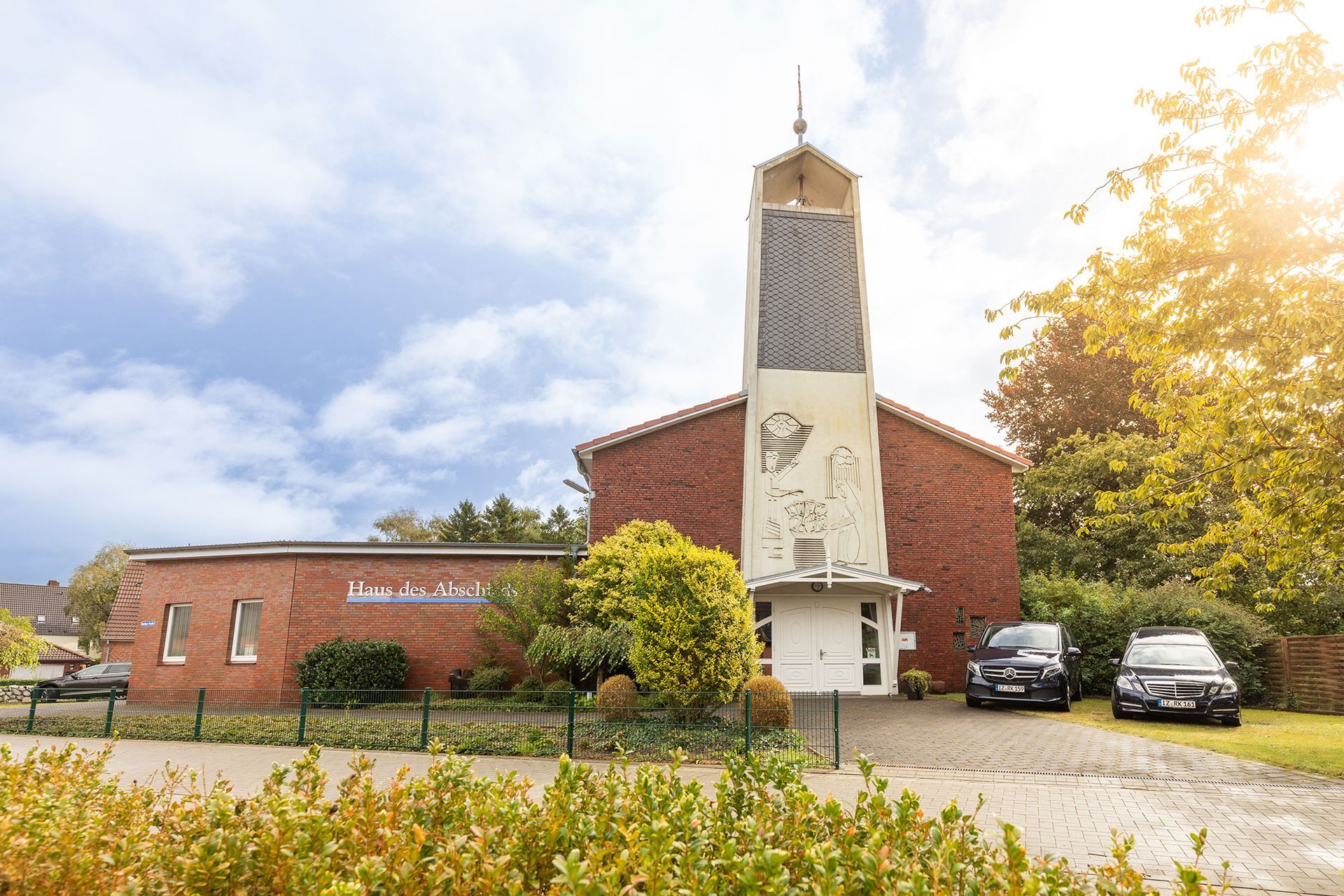 Ein rotes Backsteingebäude mit einem hohen weißen Turm, davor geparkte Autos.