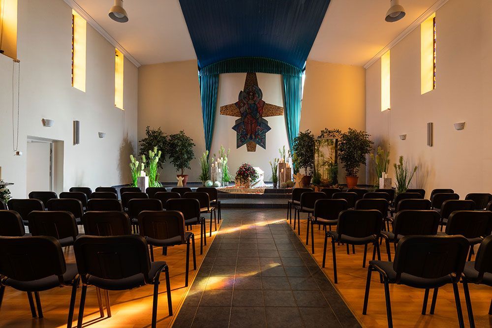 In einem hellen Raum stehen Stuhlreihen vor einem Altar. Ein farbenfrohes Kunstwerk dient als Hintergrund.
