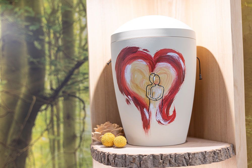 Weiße Urne mit rotem und gelbem Herzmotiv, Holzregal, Waldhintergrund.