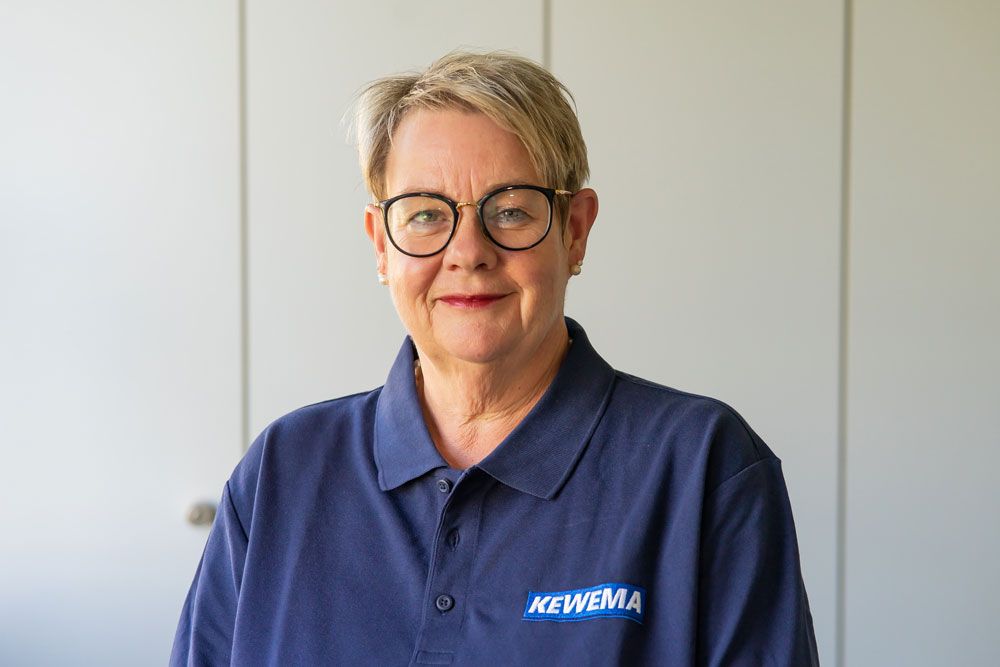 Eine Frau mit Brille und blauem Poloshirt lächelt.