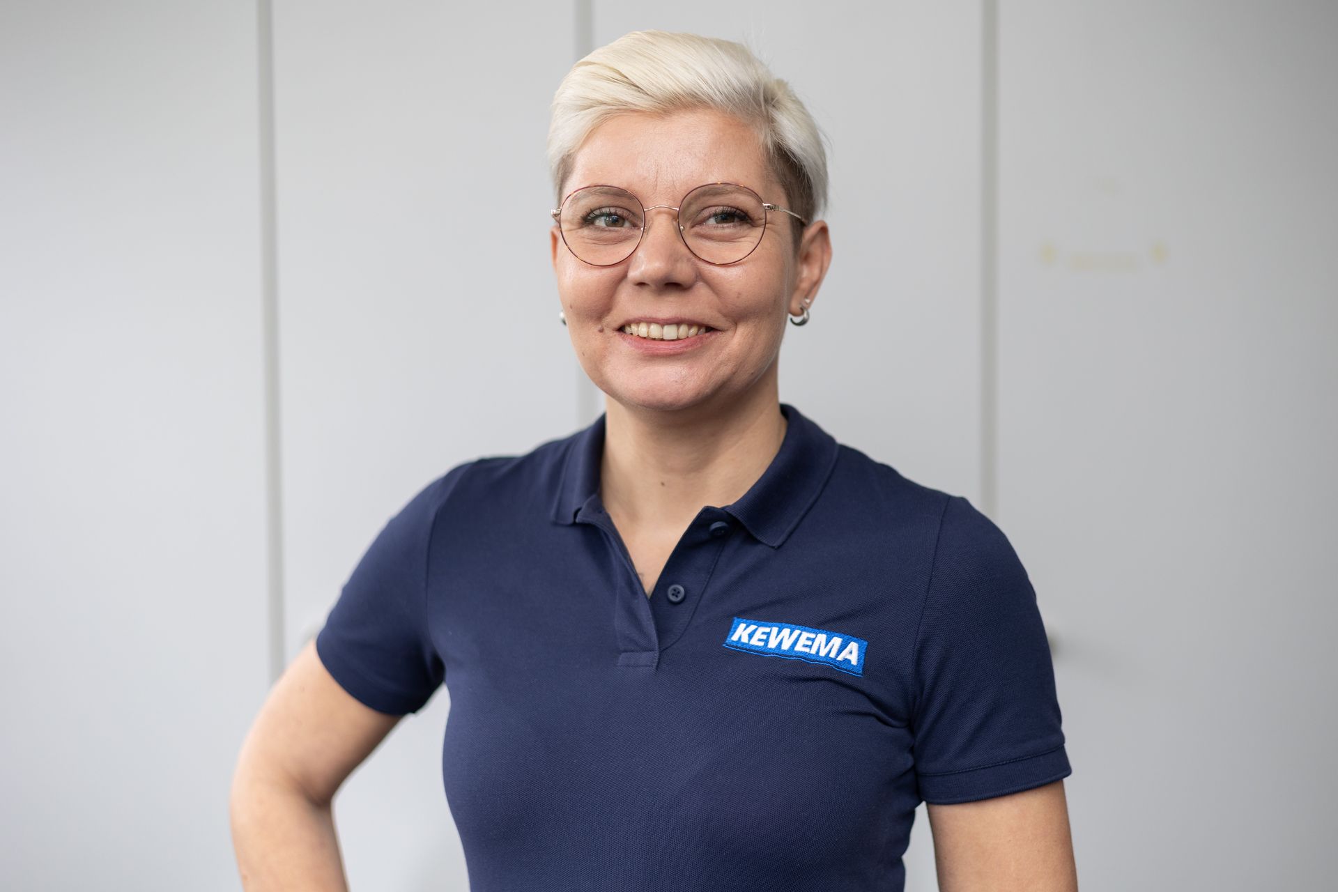 Eine Frau mit Brille und blauem Poloshirt lächelt.