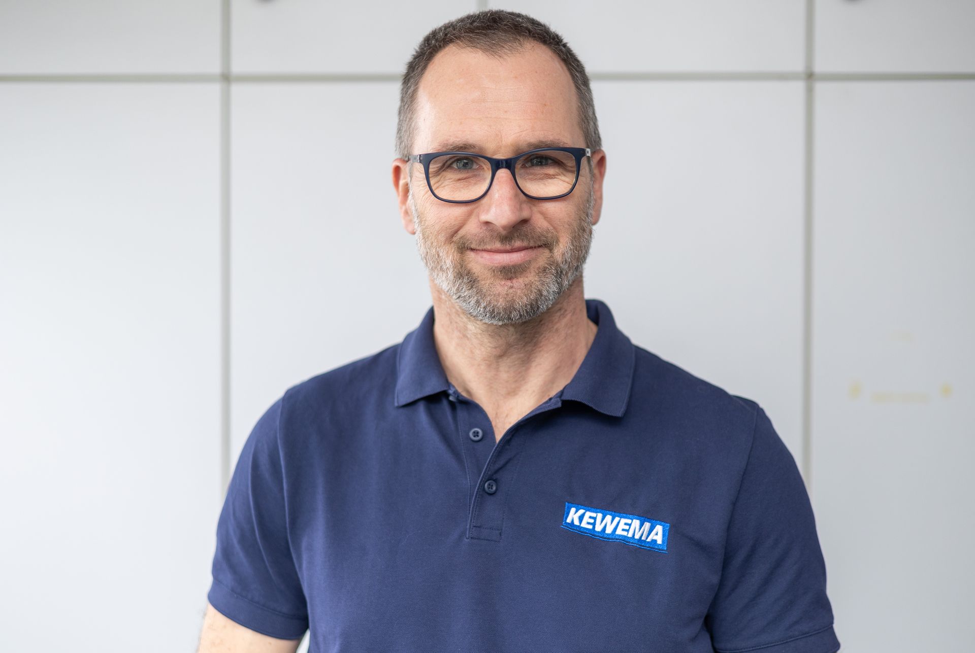 Ein Mann mit Brille und blauem Poloshirt lächelt in die Kamera.