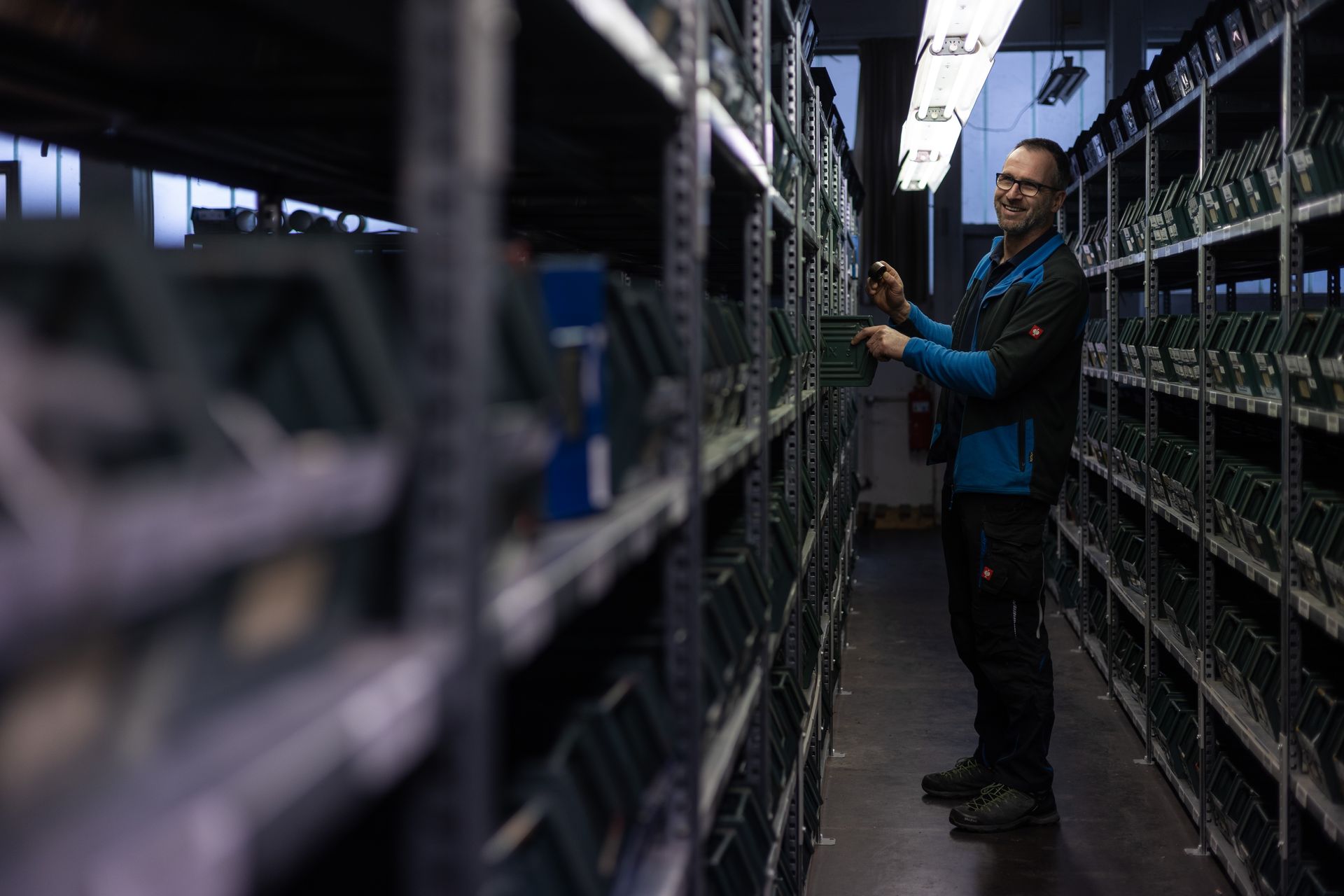 Ein Mann steht in einer Lagerhalle und schaut auf ein Telefon.
