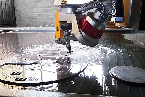 Eine Maschine schneidet ein Stück Metall mit dem Buchstaben M darauf.