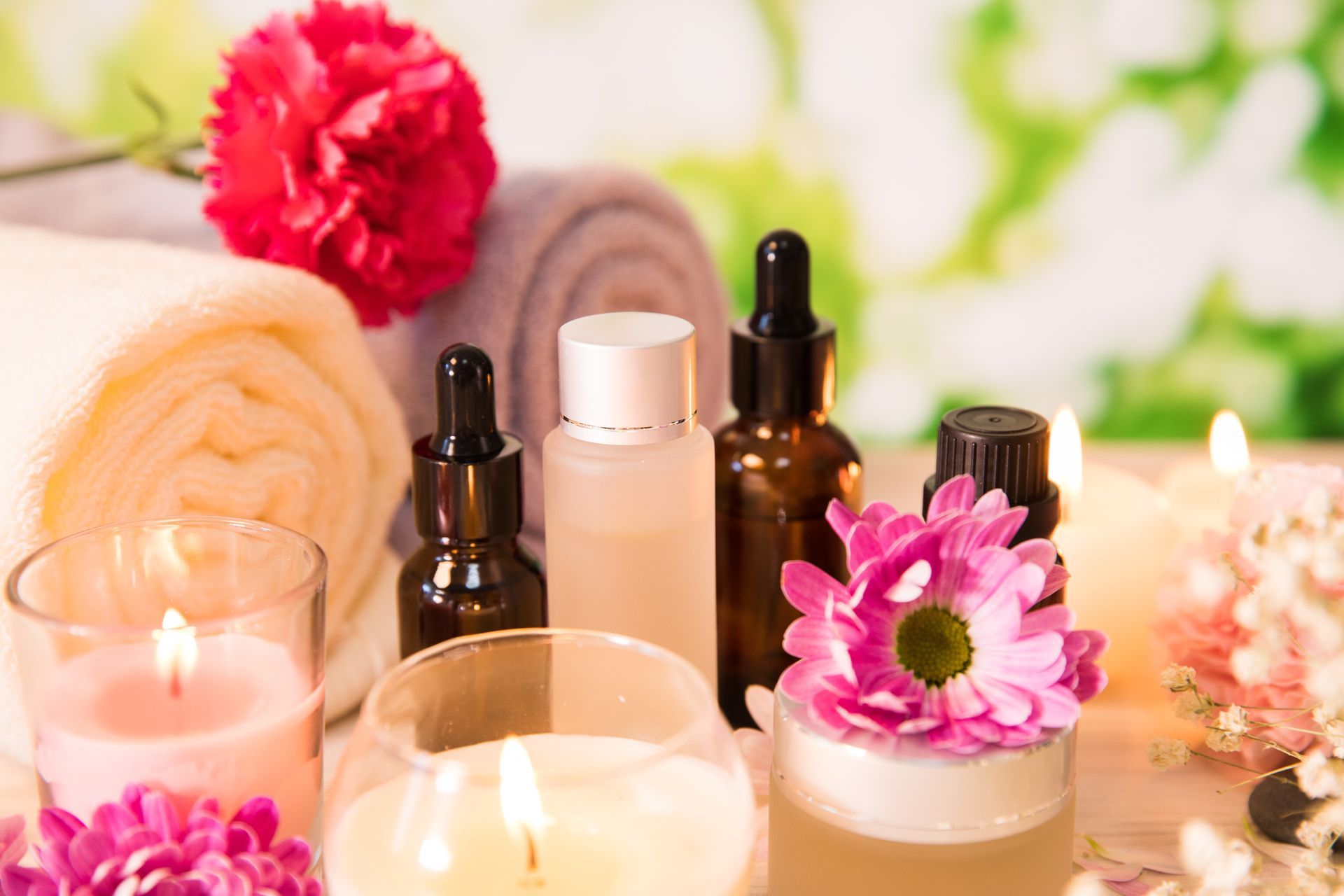 Scena spa: zwinięte ręczniki, świece, buteleczki z olejkami eterycznymi i kwiaty.