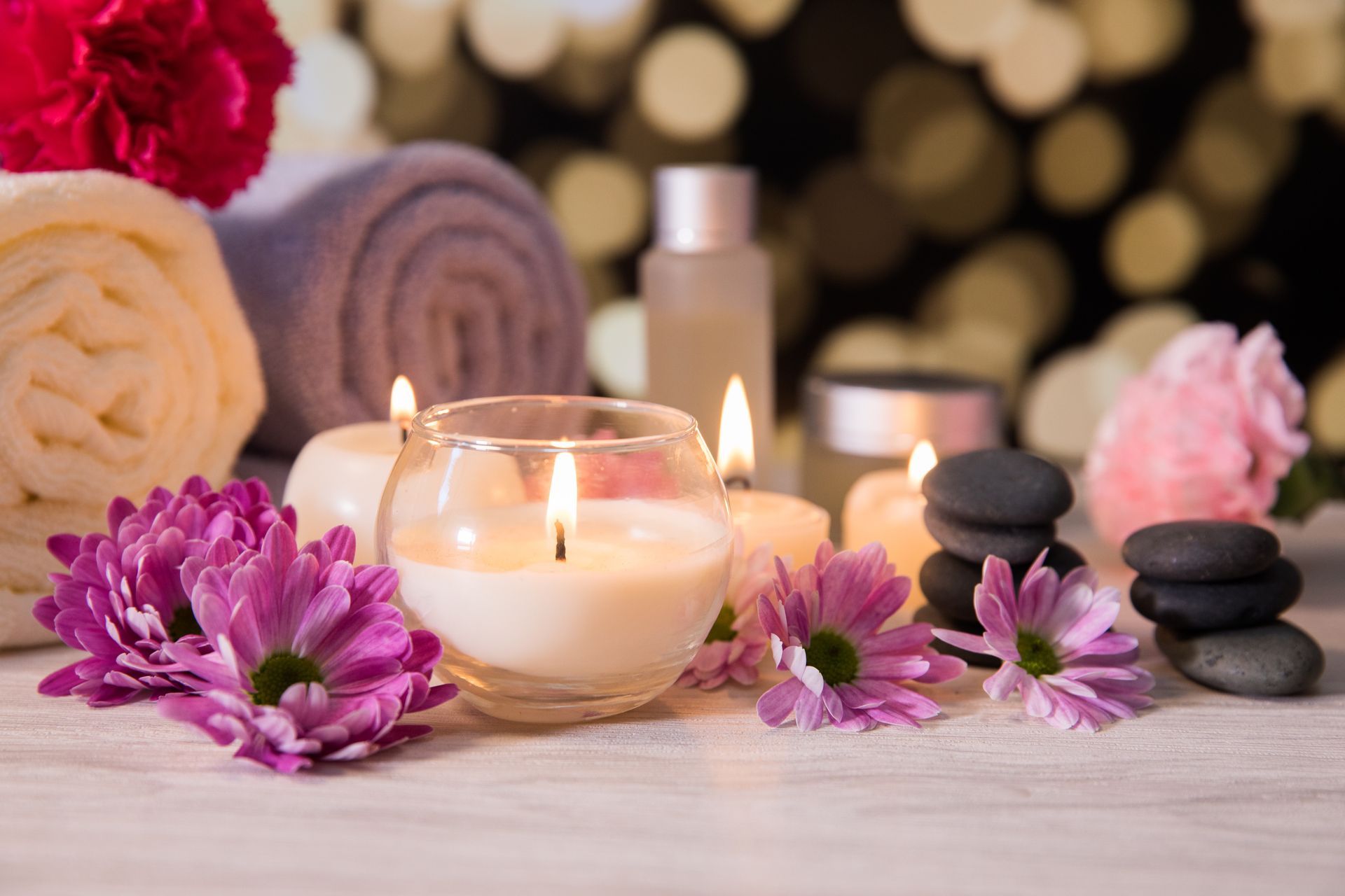 Scena spa: zapalone świece, kwiaty, ułożone kamienie, zwinięte ręczniki i kosmetyki, tworzące relaksującą atmosferę.