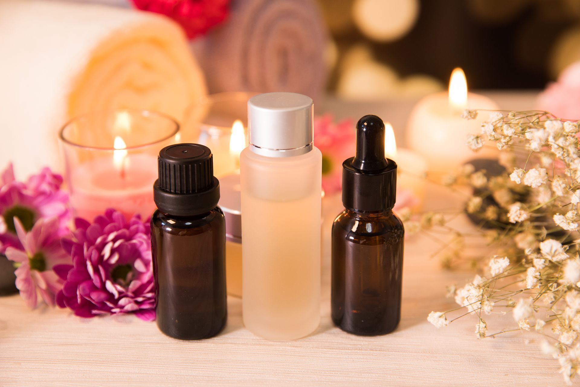 Butelki z olejkami otoczone świecami i kwiatami tworzą atmosferę relaksu i przypominają spa.