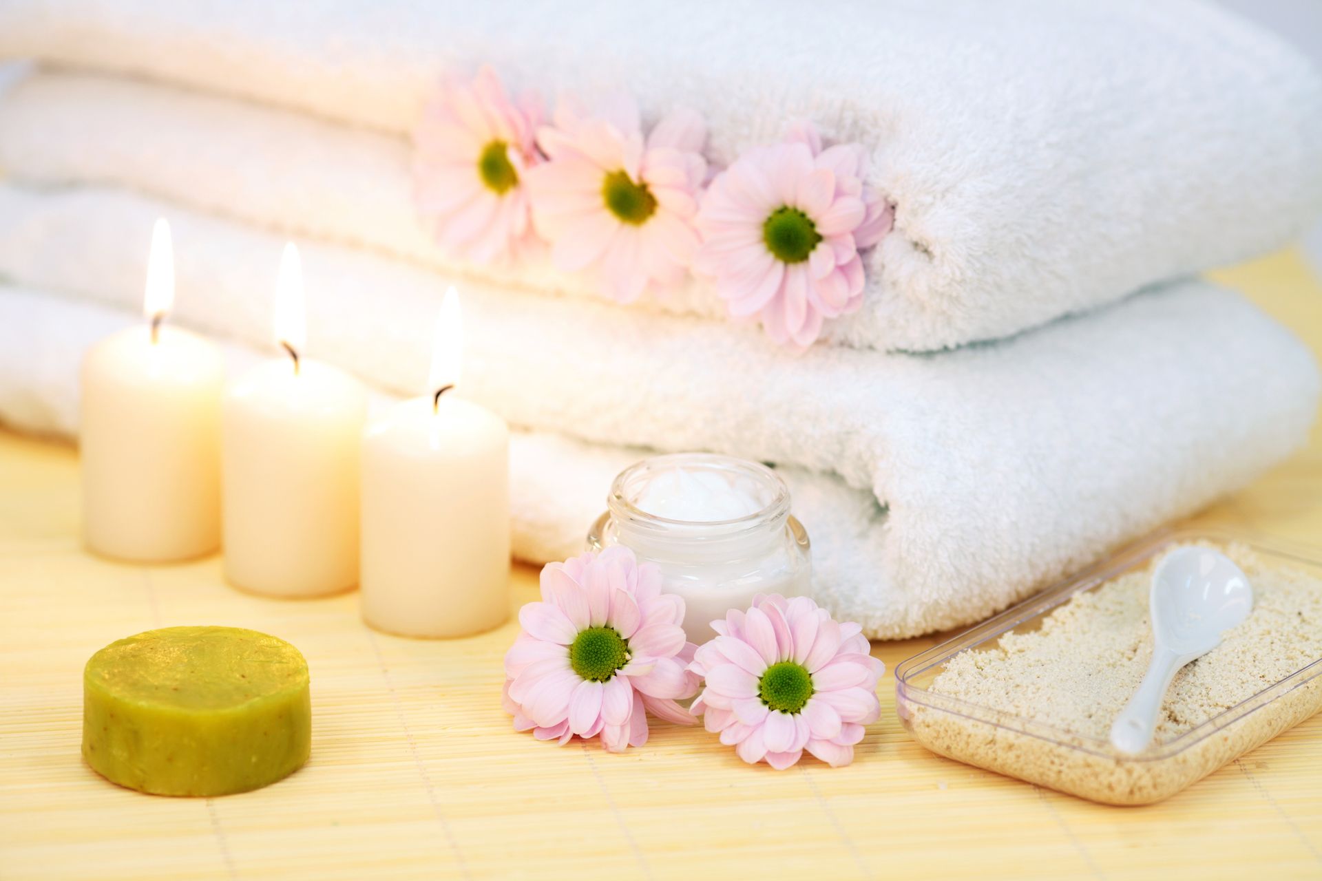 Ułożone białe ręczniki, różowe kwiaty, świece i produkty spa.