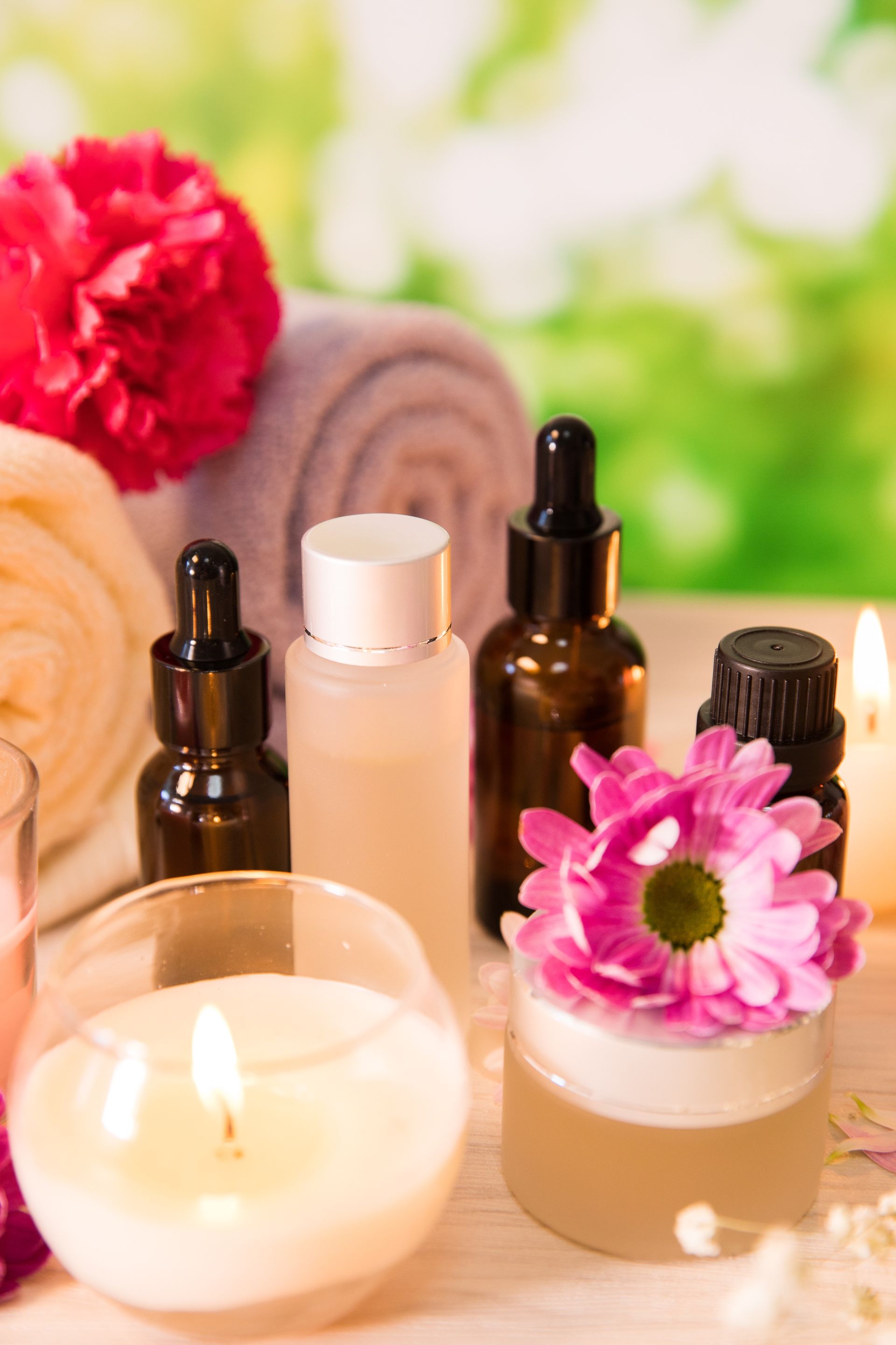 Scena spa: butelki, słoik, świece, kwiaty i zwinięte ręczniki w delikatnym oświetleniu.