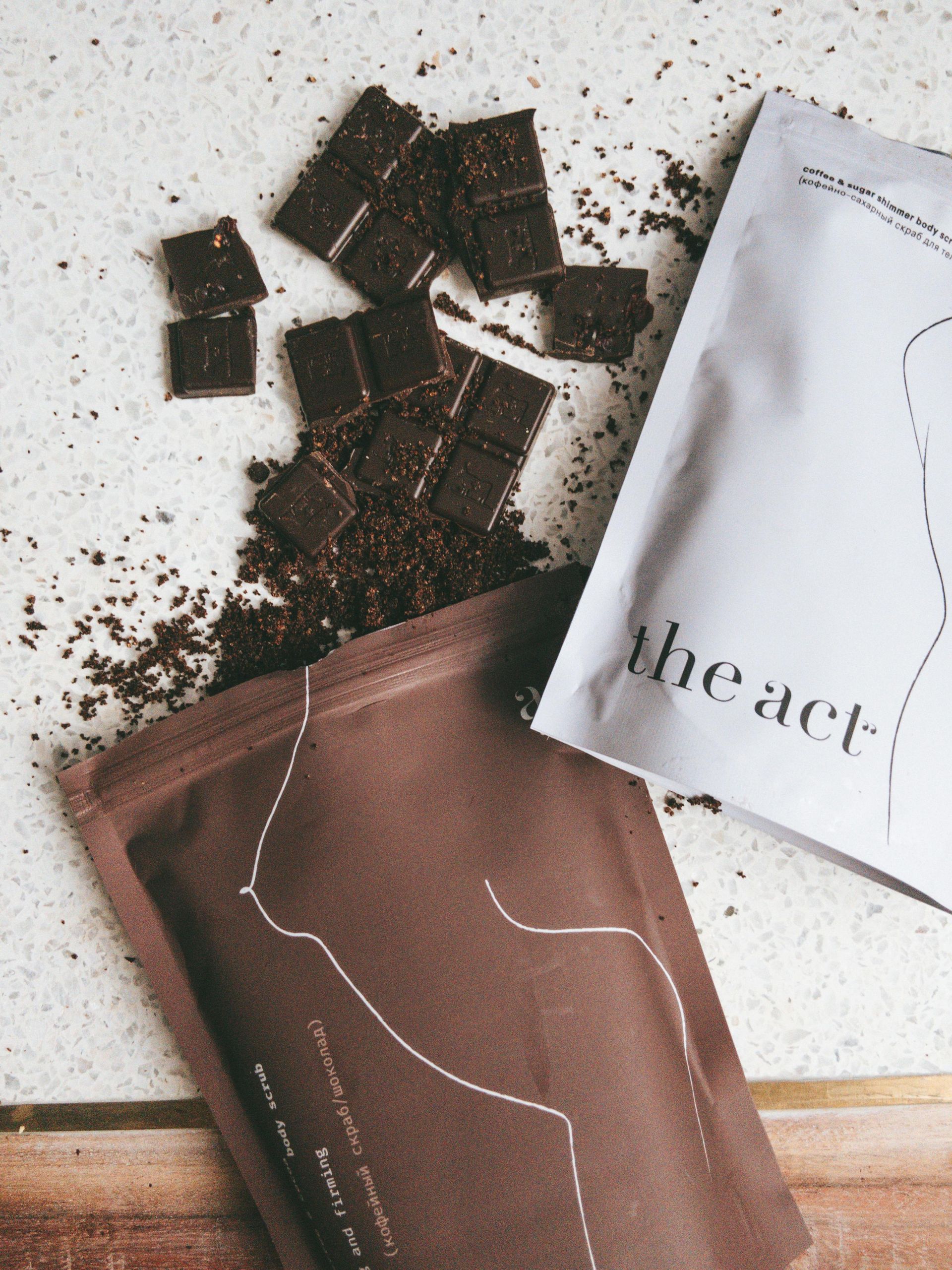 Rozbita tabliczka czekolady obok dwóch brązowo-białych opakowań produktu z etykietą „the act-”.