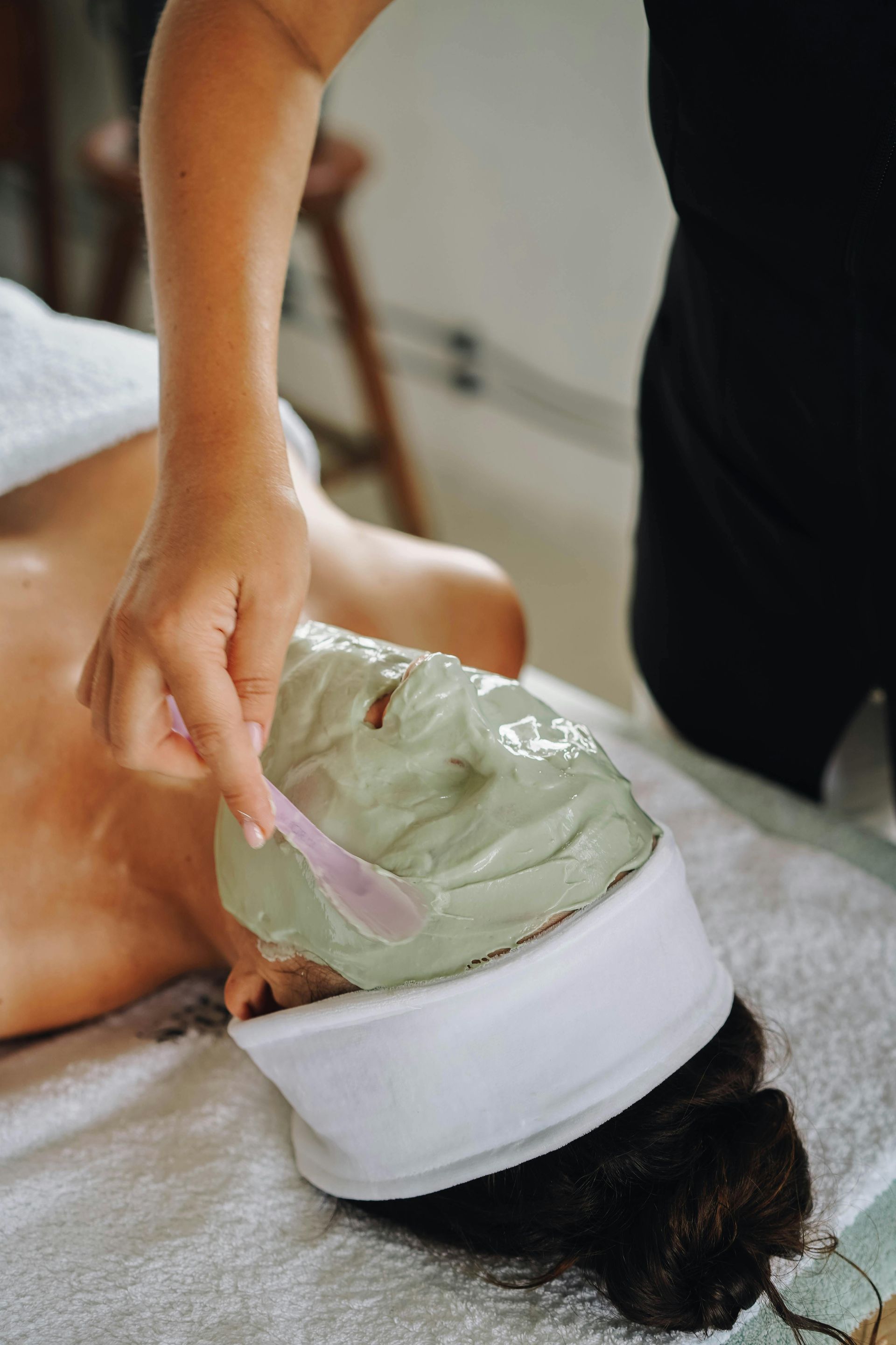 Dłonie masujące czoło osoby leżącej na stole do masażu.