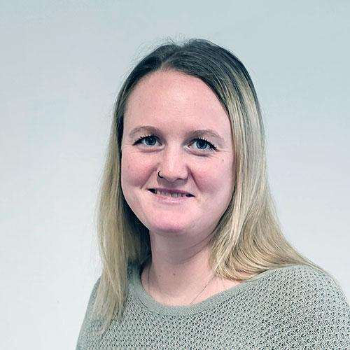 Porträt einer lächelnden Person mit blonden Haaren vor einem einfarbigen, hellen Hintergrund