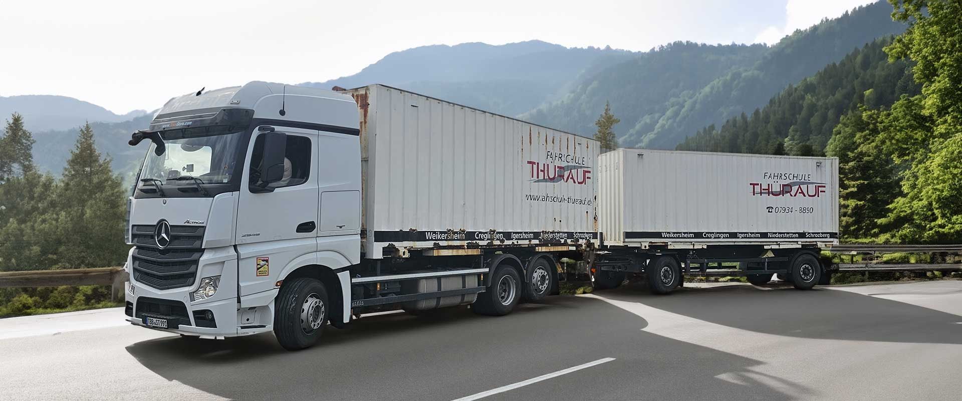 Ein weißer Sattelzug mit zwei Anhängern fährt auf einer Bergstraße unter bewölktem Himmel