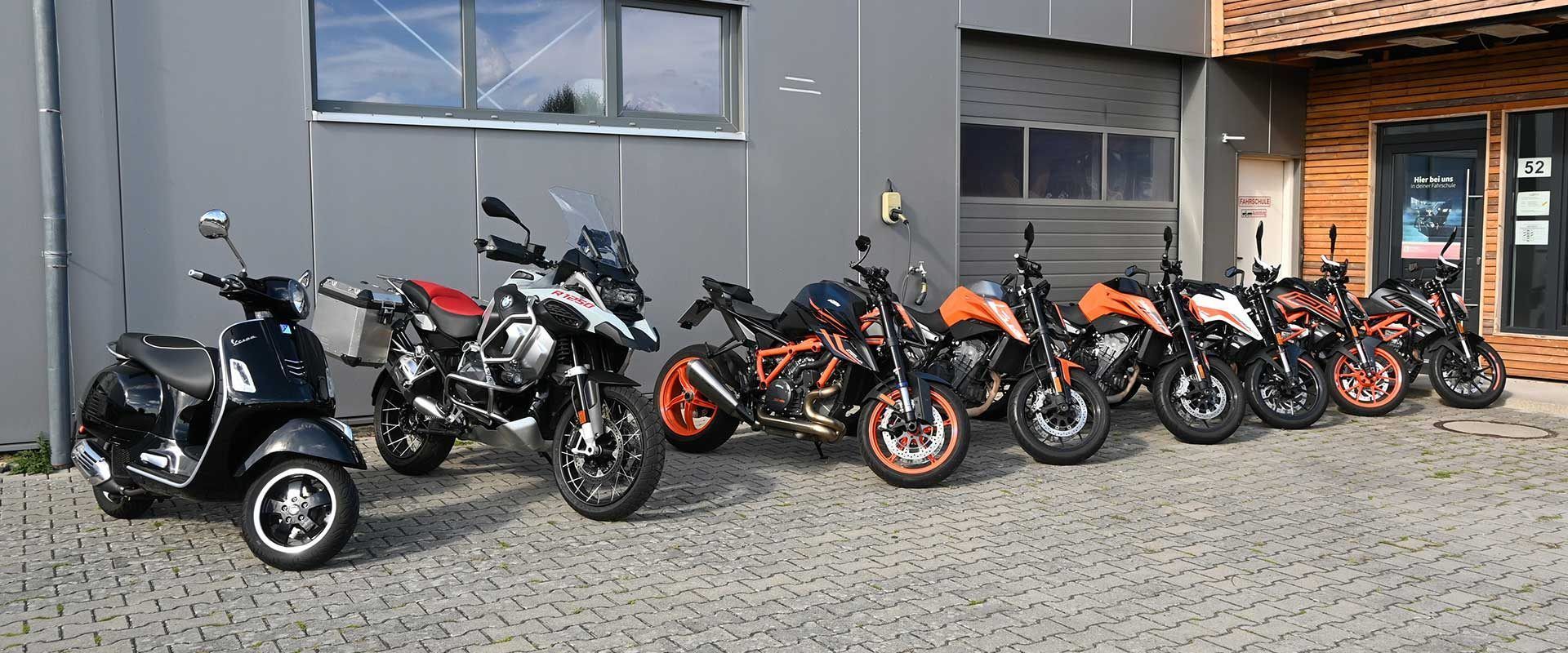 Eine Reihe geparkter Motorräder und Roller vor einem Gebäude, überwiegend schwarz mit einigen orangefarbenen Akzenten.