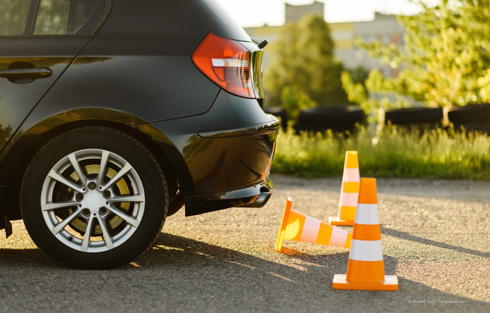 Schwarzes Auto neben zwei orangefarbenen Verkehrskegeln, neben denen ein kleines Feuer am Straßenrand brennt.