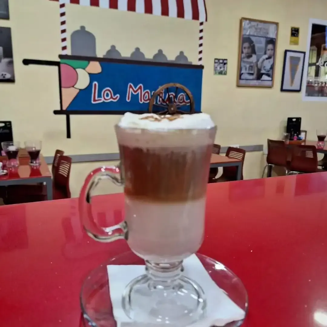 Un café con leche decorado con hojas en un platillo, junto a crepes dobladas sobre una mesa de madera.