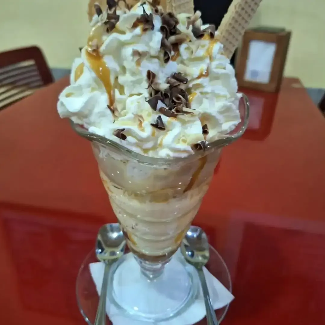 Tres bolas de helado en un tazón de madera con un cono de waffle sobre una mesa de madera oscura.