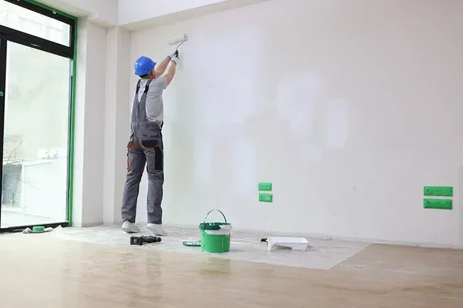 Un hombre está pintando una pared en una habitación vacía.