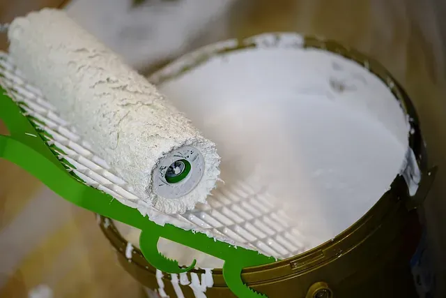 Un rodillo de pintura está colocado encima de un balde de pintura blanca.