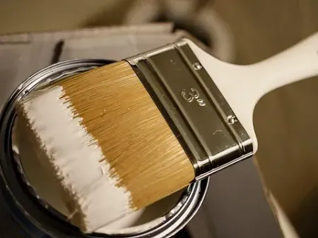 Un pincel está encima de una lata de pintura blanca.