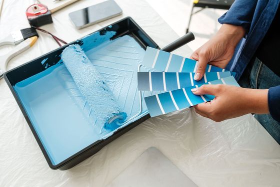 Des mains tenant des échantillons de peinture bleue au-dessus d'un plateau de peinture bleu clair sur une table de travail