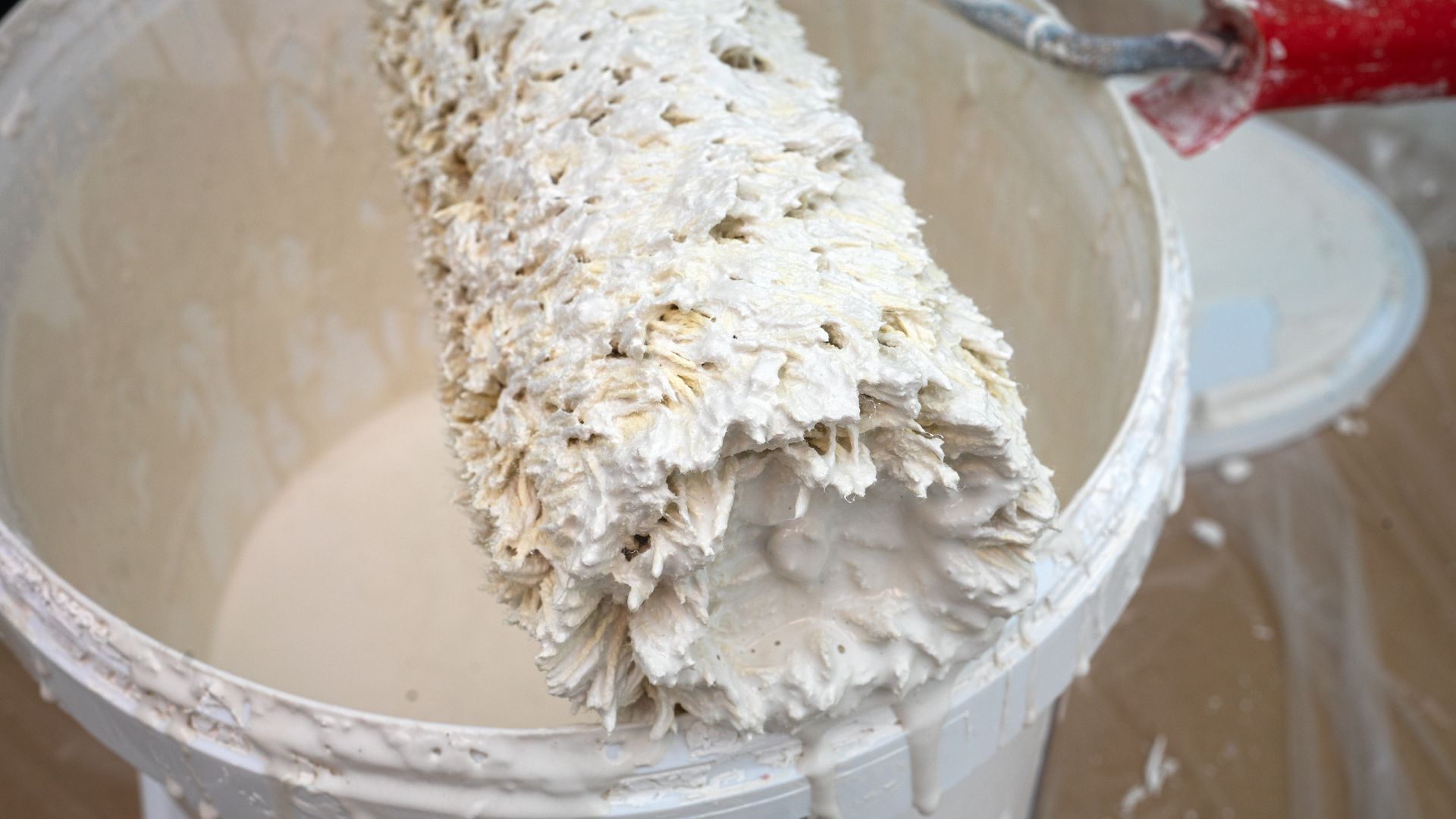 Rouleau à peinture recouvert de peinture blanche, posé dans un seau