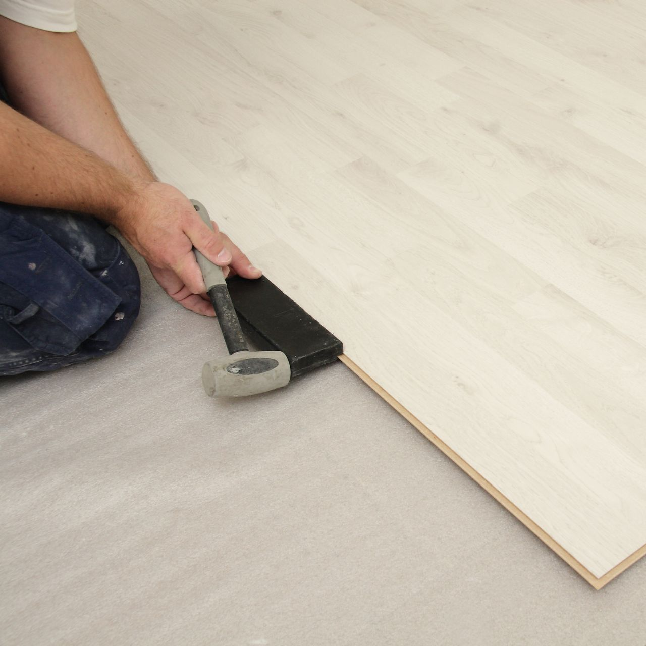 Une personne utilise un marteau pour installer une planche de parquet clair