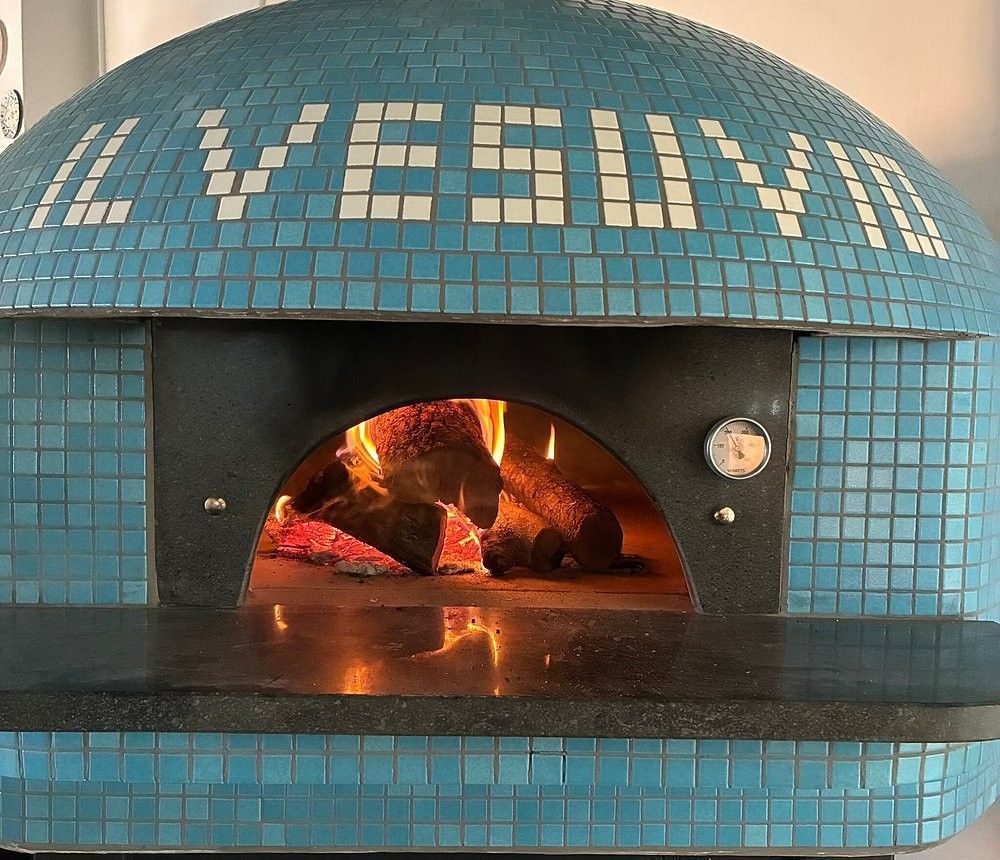 Horno de pizza Il Vesuvio con azulejos azules y leña encendida en su interior.