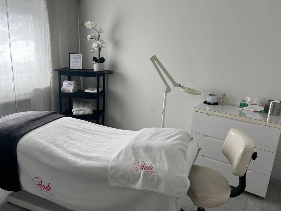 Salle de soins esthétiques : lit blanc, petite table noire, lampe, armoire blanche.