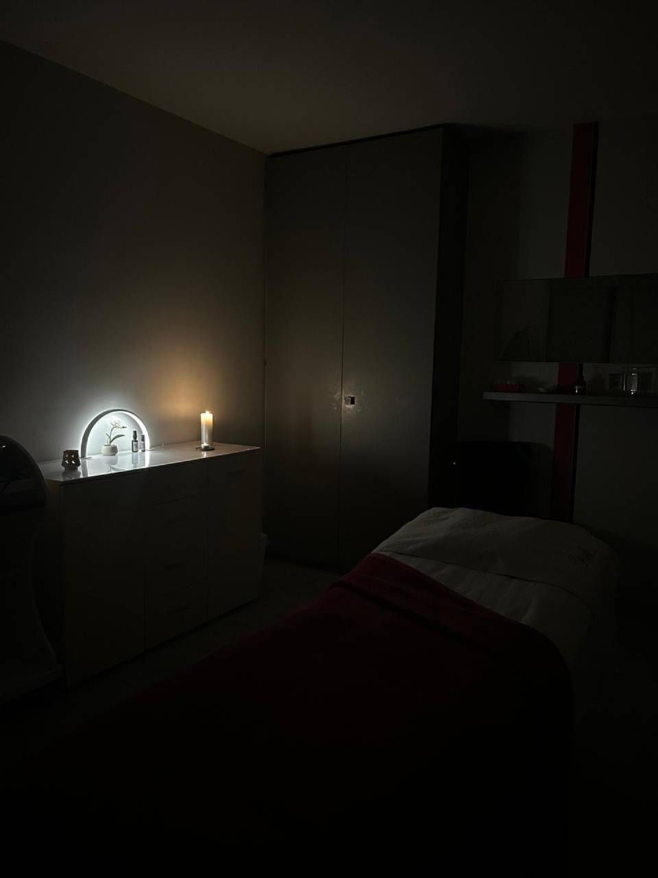 Salle de massage faiblement éclairée avec une bougie, une table de massage et une armoire.