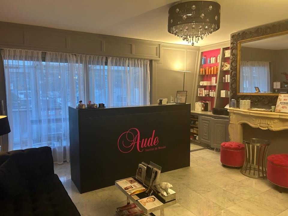 Espace d'accueil d'un salon de beauté avec un comptoir noir affichant « Aude ». 