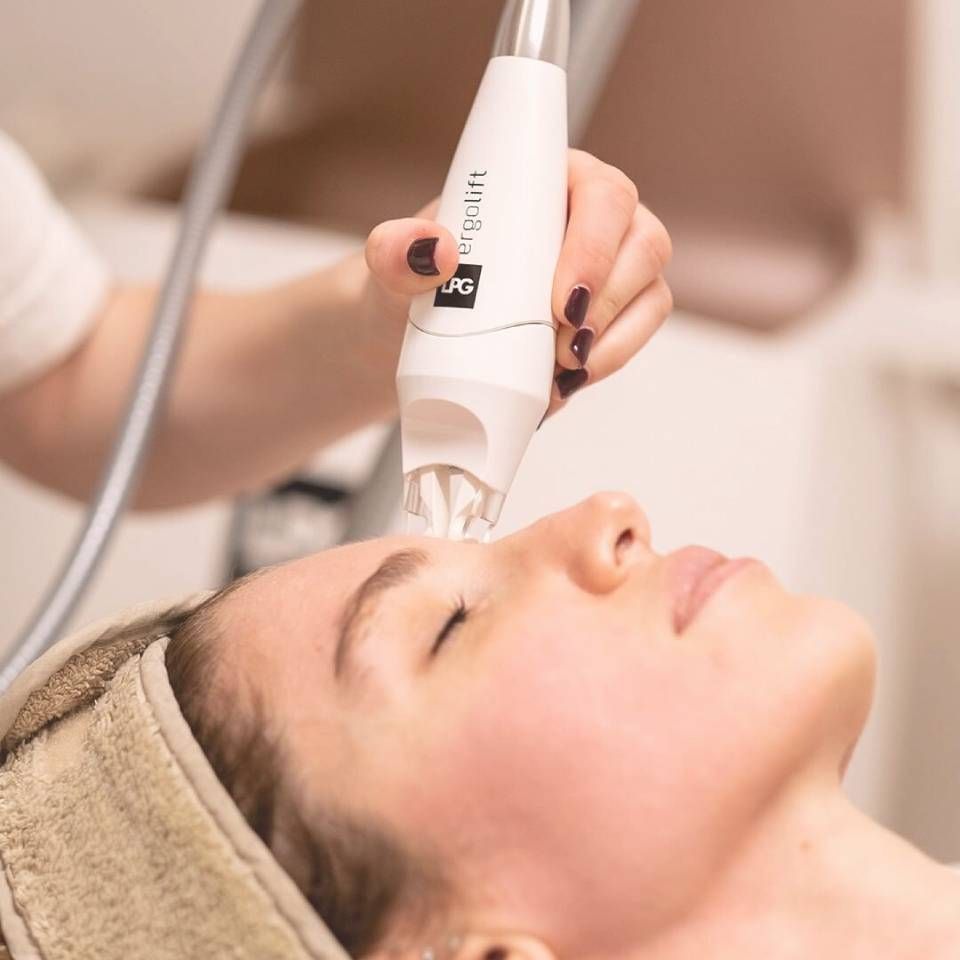 Personne recevant un soin du visage avec un appareil portatif ; le lieu est un spa ou une clinique.