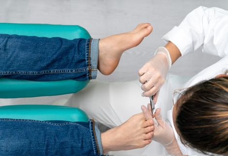 Persona cortándose las uñas de los pies en un salón. El técnico lleva guantes y bata blanca.