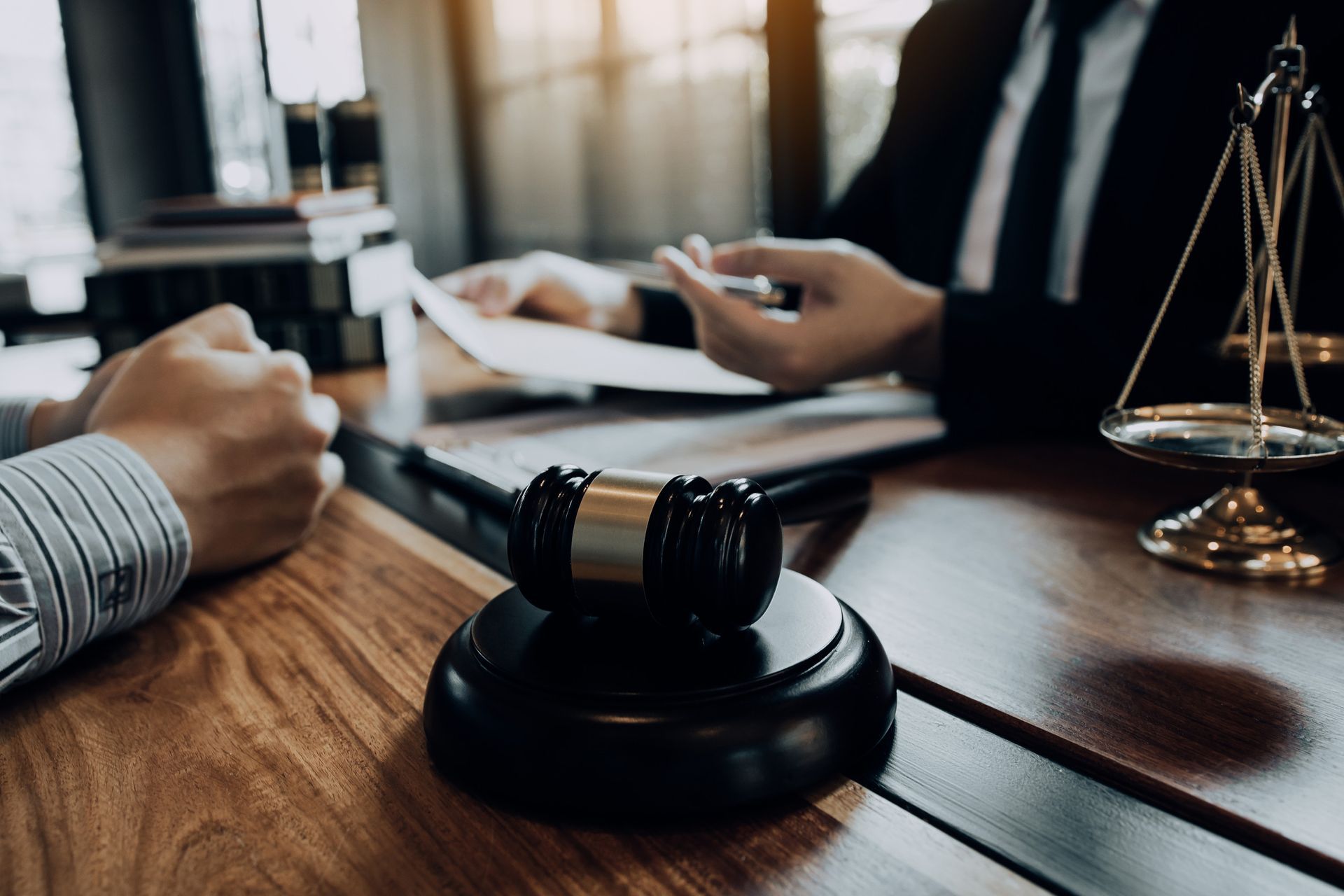 Abogado y cliente discuten documentos sobre una mesa con un mazo y una balanza de la justicia.