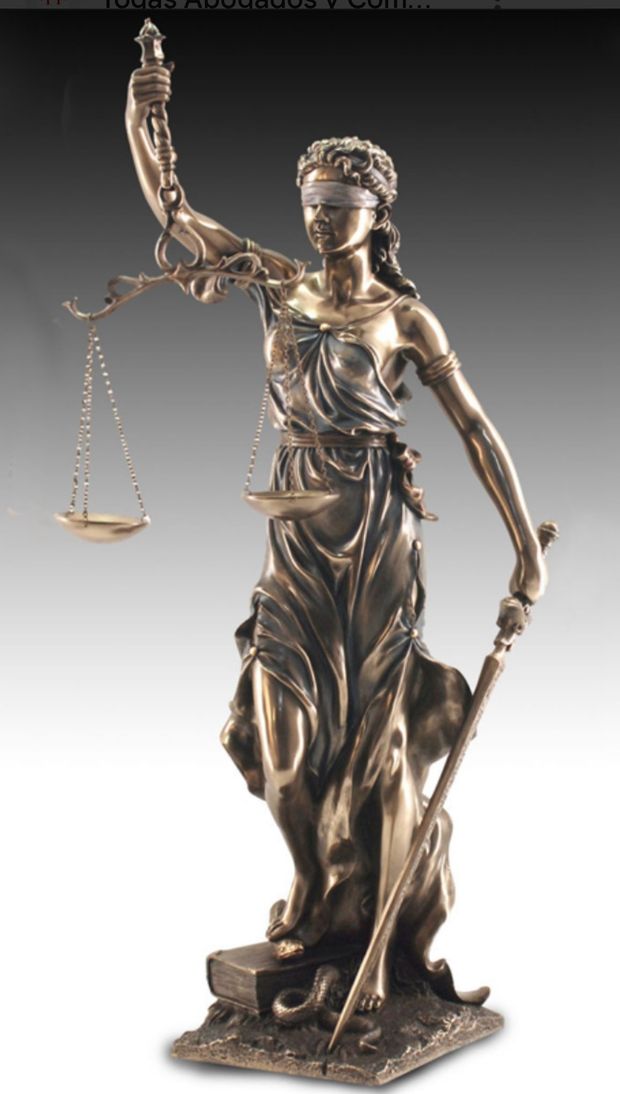 Balanza dorada de la justicia sobre un escritorio, con una persona y una tableta en el fondo.