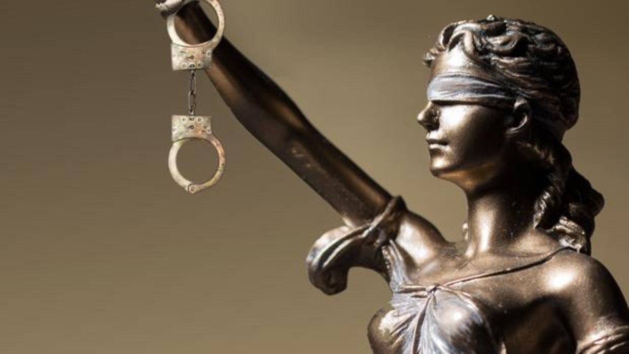 Balanza dorada de la justicia sobre un escritorio, con un abogado borroso en el fondo.