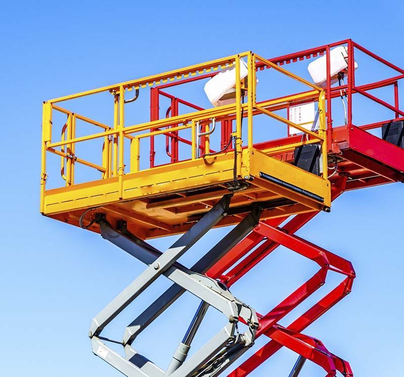 Plataforma elevadora de tijera roja y amarilla extendida contra un cielo azul