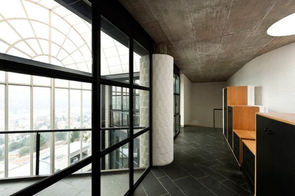 Pasillo interior moderno con grandes ventanales arqueados, barandilla negra y armarios de madera a la derecha.