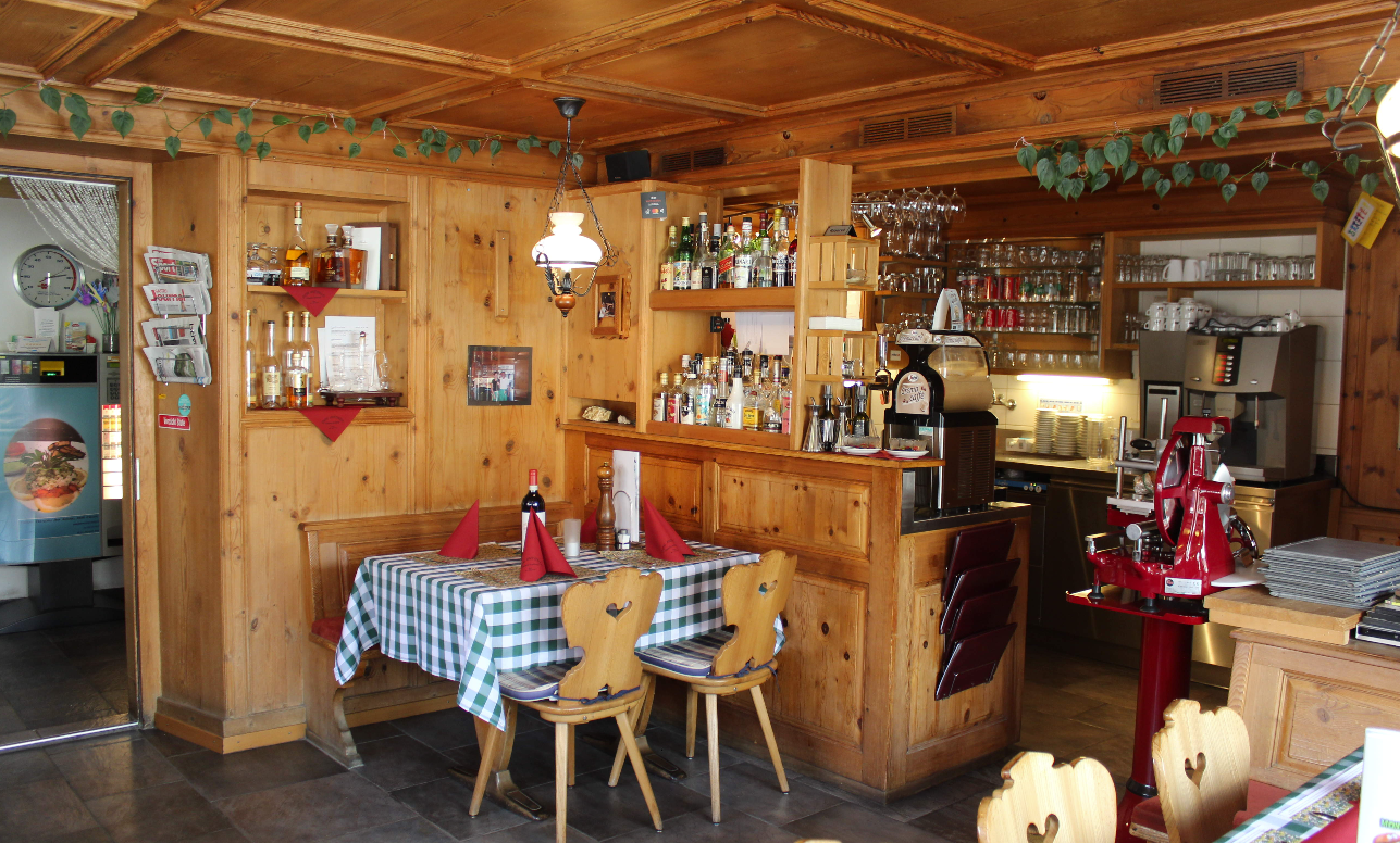 Gemütliches, rustikales Barinterieur mit Holzdekor, karierten Tischdecken und Flaschenregalen hinter der Theke.