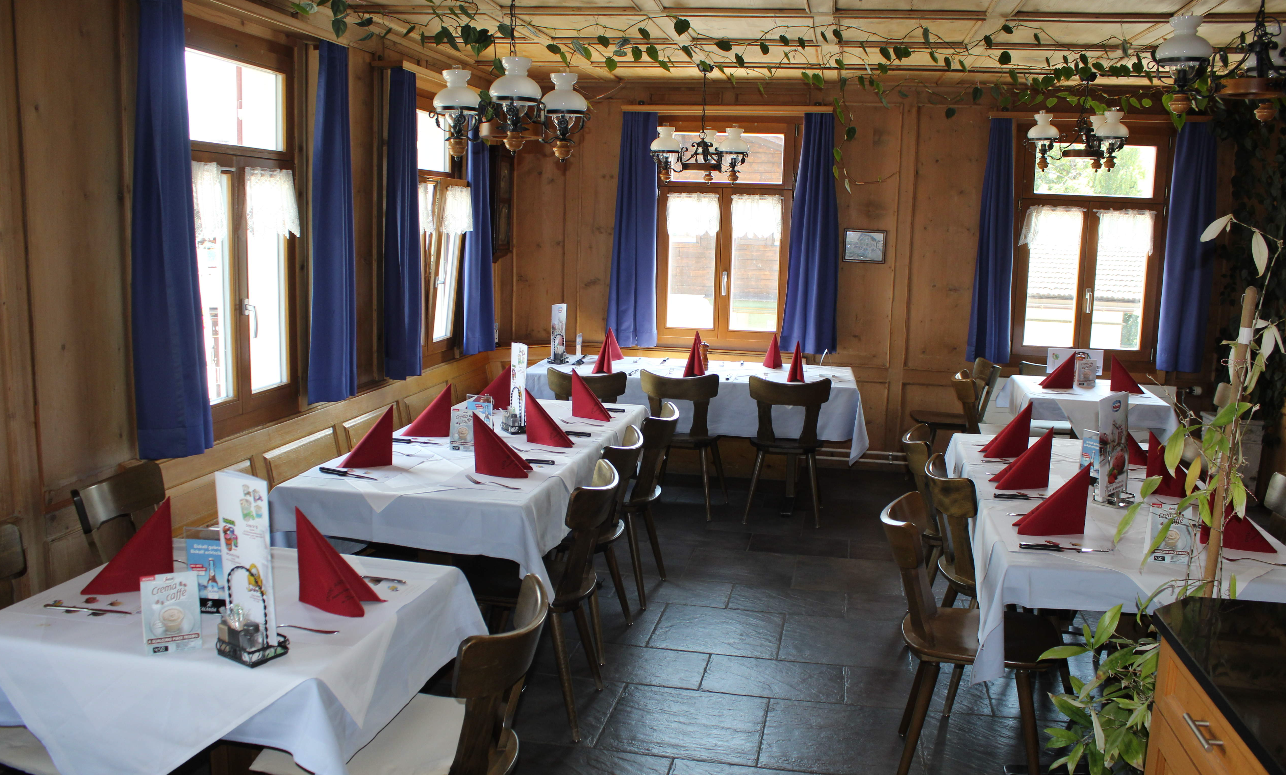 Gemütlicher Speisesaal mit weissen Tischdecken, roten Servietten und grossen Fenstern mit blauen Vorhängen