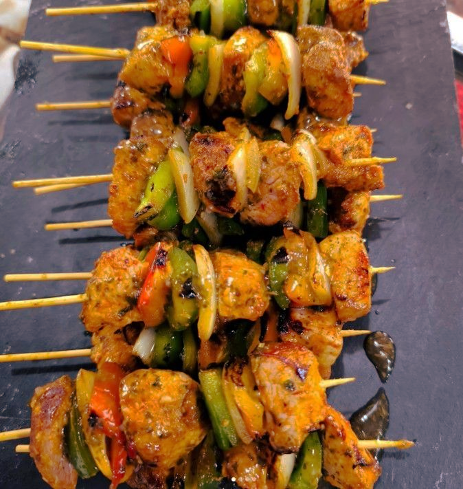 Brochetas de pollo a la parrilla, pimientos y cebollas, dispuestas sobre una superficie oscura.