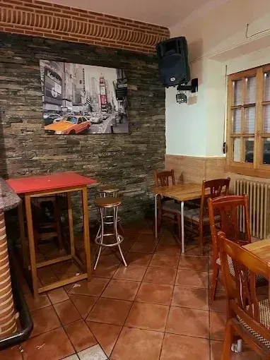 Interior de un pequeño restaurante con mesas, sillas, pared con acento de ladrillo y una foto de la ciudad de Nueva York en la pared.