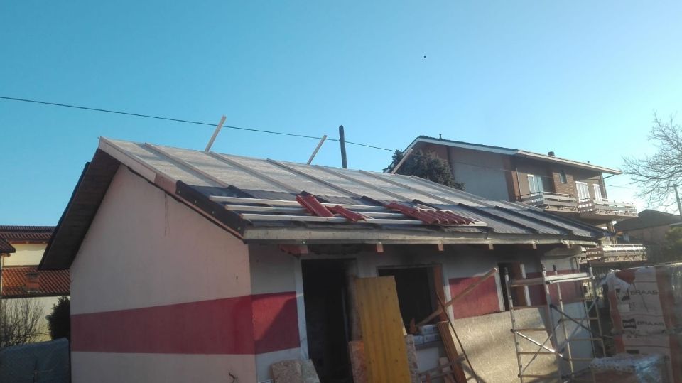 Un piccolo edificio in costruzione con tetto parzialmente coperto e dipinto di rosso e bianco.