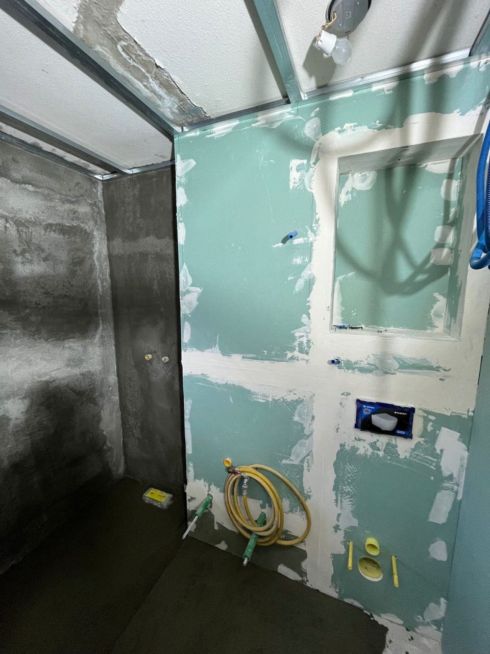 Bagno in costruzione; cartongesso verde, tubature a vista e struttura metallica.