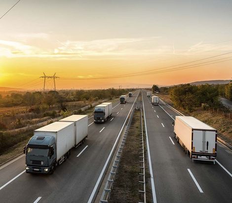 Camiones circulando por una autopista al atardecer, con un cielo anaranjado y un paisaje abierto