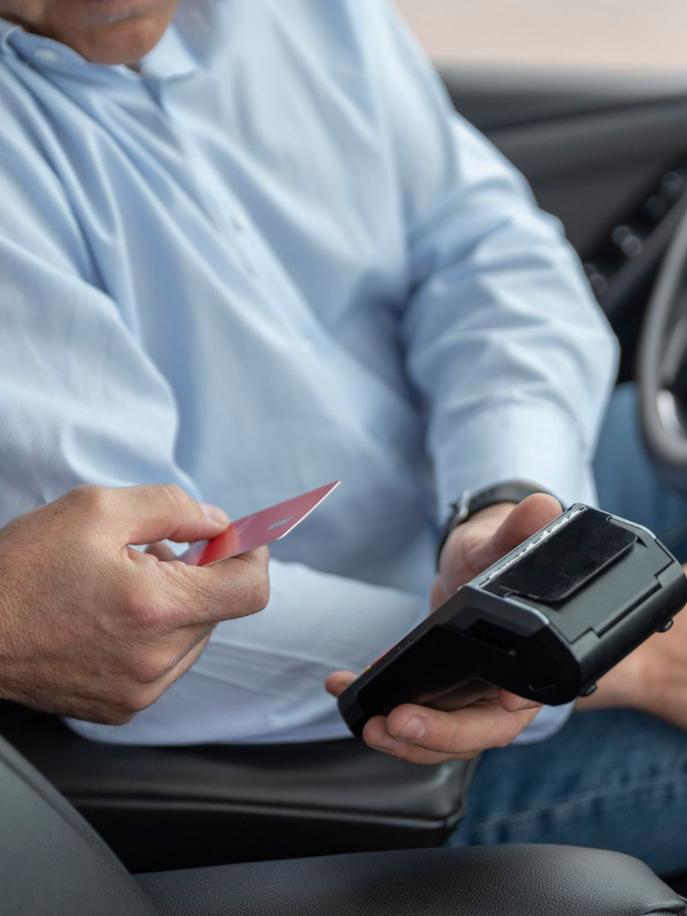 Personne dans une voiture tenant une carte de crédit près d'un terminal de paiement, payant un service.