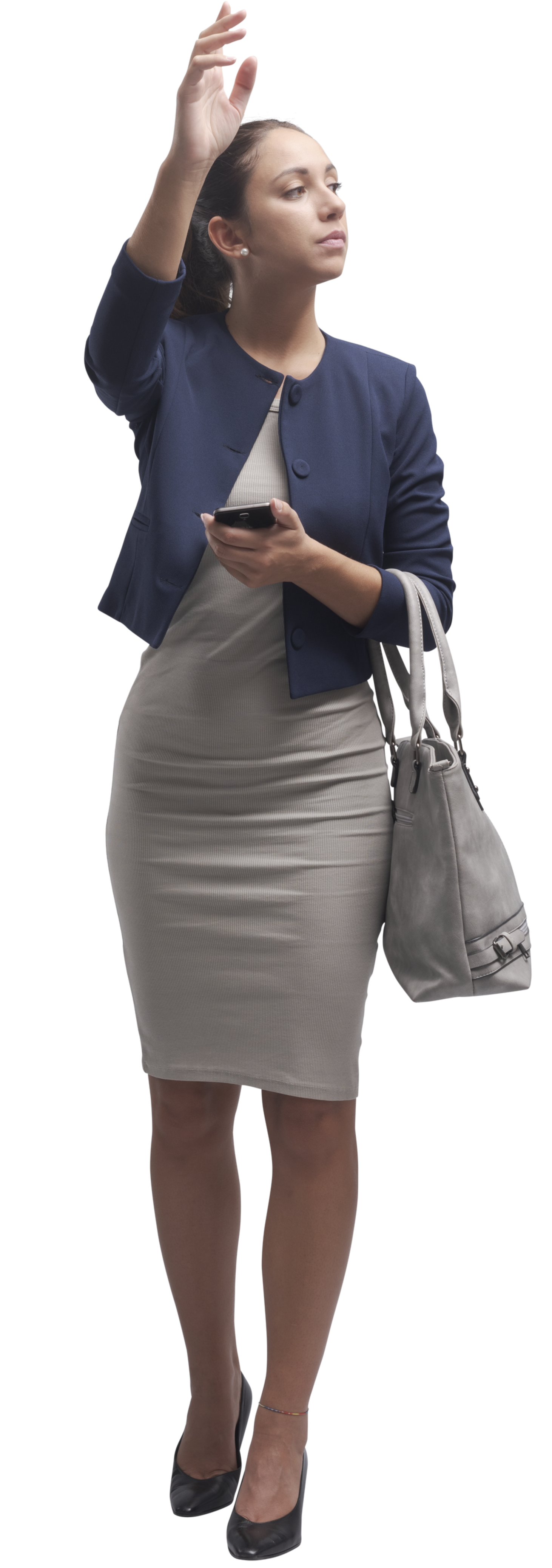 Femme vêtue d'une veste bleue et d'une robe grise, levant la main pour saluer quelque chose, tenant un téléphone et un sac.