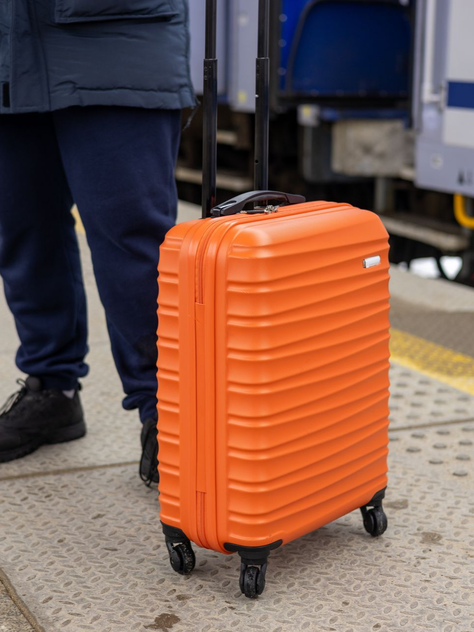 Une personne tenant une valise à roulettes orange sur le quai d'une gare.